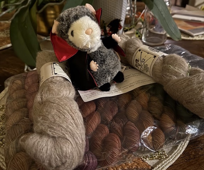 A vampire possum stuffed animal on top of a package of yarn